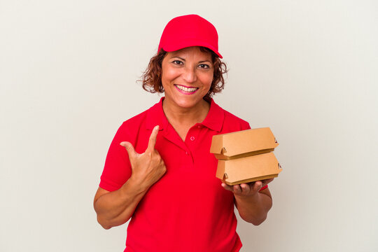 Middle age delivery woman taking burguers isolated on white background pointing with finger at you as if inviting come closer.