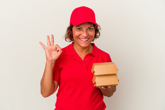 Middle age delivery woman taking burguers isolated on white background cheerful and confident showing ok gesture.