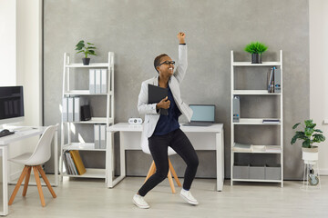 Excited carefree business woman holding office papers, dancing and having fun during break at work.Funny happy modern short haired active young girl feeling free from responsibility as vacation starts - obrazy, fototapety, plakaty