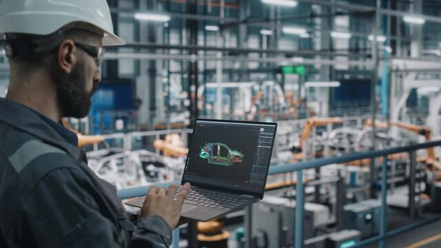 Car Factory Engineer in Work Uniform Using Laptop Computer with Digital 3D CAD Vehicle Blueprint. Male Specialist in Automotive Industrial Manufacturing Facility Working on Automobile Production.