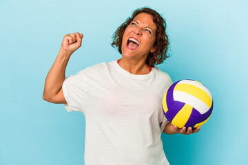 Middle age latin woman playing volleyball isolated on blue background raising fist after a victory, winner concept.