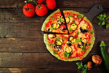 Healthy, gluten free green vegetable crust pizza with tomatoes, zucchini and mushrooms. Top down view with cut slices. Table scene on a dark wood background.