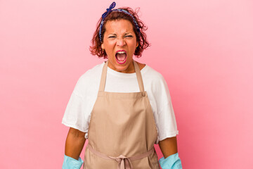 Middle age latin woman isolated on pink background screaming very angry and aggressive.