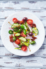 Simple Salad with Green and Kalamata Olives, Cucumber, Cherry and marinated Tomatoes, Capers and Jalapeno Pepper. Bright wooden background. Top view.  