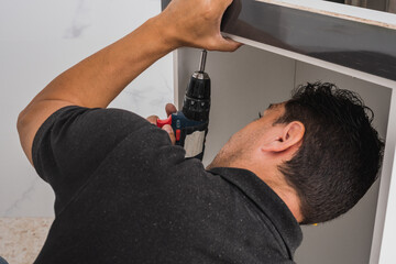 Man bent over while using a drill to assemble a kitchen unit