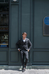 Handsome businessman in black formal suit standing on dark green background. Model posing. High quality photo