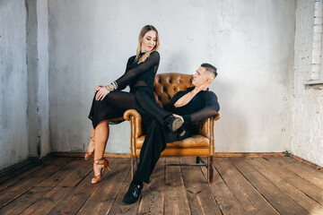 Portrait of Couple two professional ballroom dancers in loft studio on Brown leather sofa. Sport life concept. Passion and emotional dance.