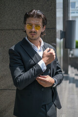 Handsome man in black formal suit and yellow sunglasses standing on the street.High quality photo