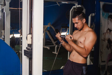 Young athletic guy training biceps with a machine at the gym.