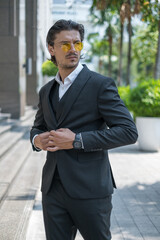 Portrait of handsome young man in black formal suit and yellow sunglasses looking aside. High quality photo