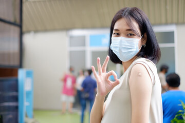 A pregnant Asian mother in a long gown is standing to show her okay gesture and showing plaster after receiving the vaccination.