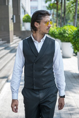Portrait of handsome young man in black formal suit and yellow sunglasses walking on the street and looking aside. High quality photo