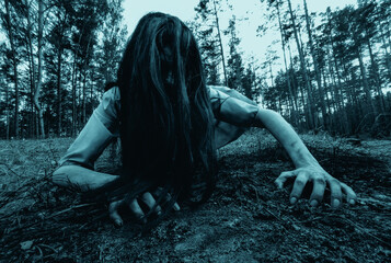 Girl in image of scary zombie crawls on ground in dark forest.