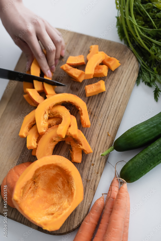 Wall mural partial view of woman cutting ripe pumpkin on chopping board near fresh carrots and cucumbers.