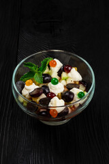 Salad from grapes apples pears kiwi oranges with mascarpone chease and cream. Healthy fresh fruit summer salad in glass bowl on black wooden background with copy space.