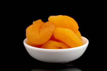Several dried organic dried apricots in a white dish, close-up, isolated on black.

