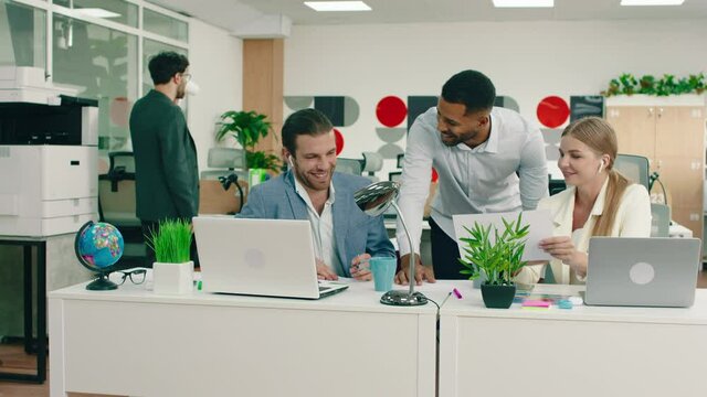 Three co- workers are having a fun conversation at work in the office, while they are laughing their manager shows up and one of them leaves, they start working again