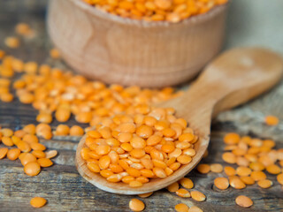Red lentils in a wooden plate and spoon on an old rustic table. Vegetarian food.