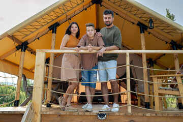 Fototapeta premium Young husband and wife and their adolescent son enjoying summer vacation by glamping house
