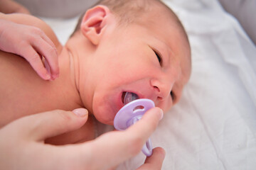 A newborn baby in a diaper is crying with a pacifier in his mouth. Child boy in a cocoon on a crib.