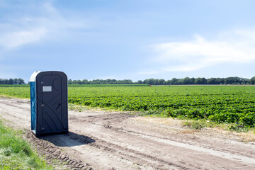 Public plastic portable toilet on agriculture field of farmer landscape with blue sky, outdoors