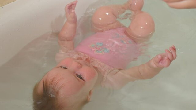 Swimming lesson for baby at home. Toddler practice diving with help parent's hand in tub. Development of the ability to hold breath underwater.