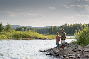 Fototapeta na wymiar Father and son standing by lake while enjoying summer vacation in the country