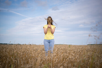 Woman a farmer hides her face behind a heap of wheat ears on a wheat field background.