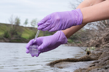 Water pollution concept. Woman a scientist takes a water sample from a river close up. - obrazy, fototapety, plakaty