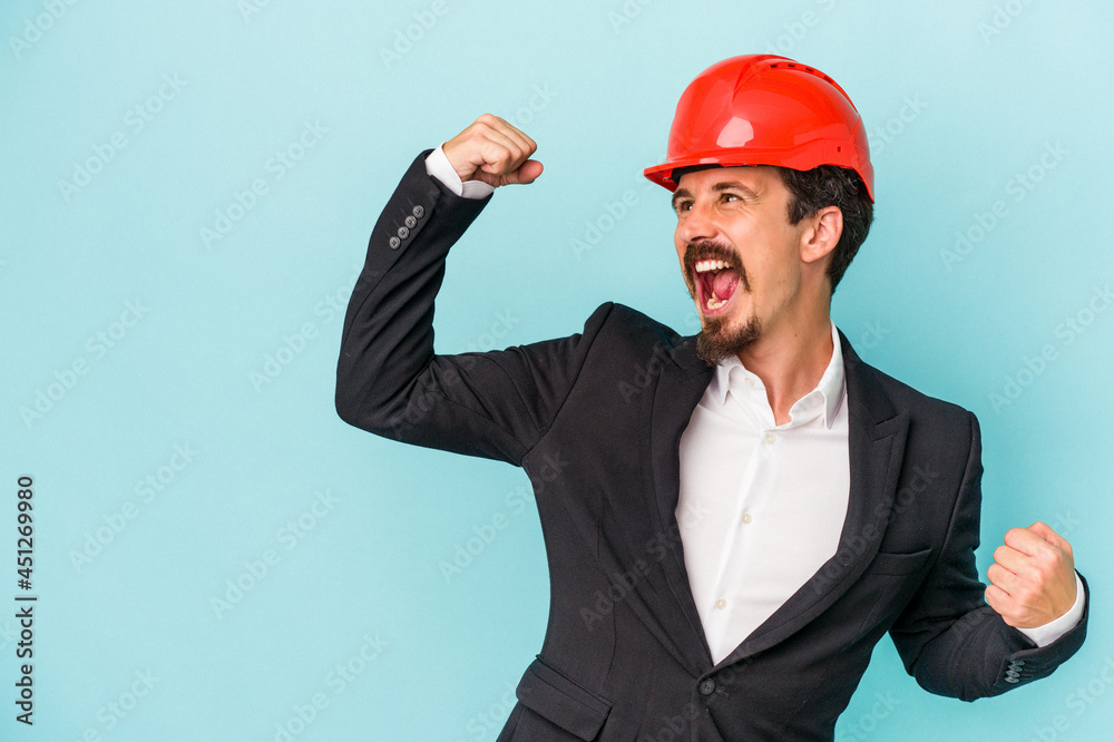 Wall mural young architect caucasian man isolated on blue background raising fist after a victory, winner conce