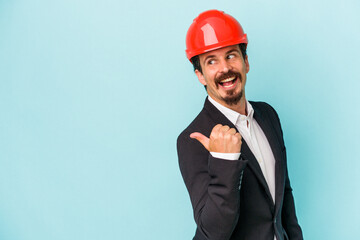 Young architect caucasian man isolated on blue background points with thumb finger away, laughing and carefree.