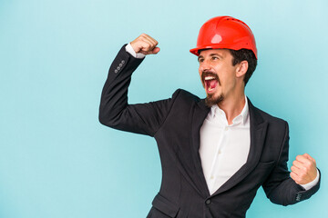 Young architect caucasian man isolated on blue background raising fist after a victory, winner concept.