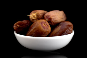 Several dried organic dates in a white saucer, close-up, isolated on black.