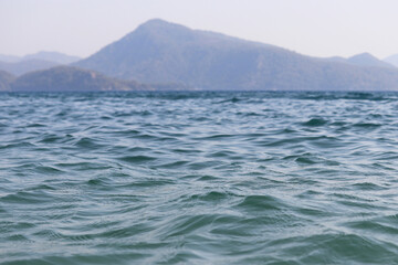Scenic view from sea water surface to mountains covered with forest in fog. Beach vacation, background for summer travel