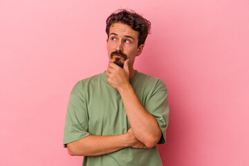Young caucasian man isolated on pink background thinking and looking up, being reflective, contemplating, having a fantasy.