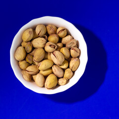 Pistachios in a white plate on blue background