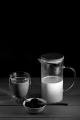 black coffee in glass cup with double walls. Milk decanter. Wooden table and black table. Coffee beans in a white plate. Black and white photo