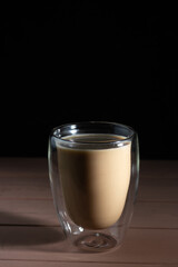 Black coffee in glass cup with double walls with milk. Wooden table and black background.
