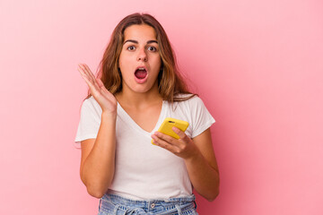 Obraz premium Young caucasian woman using mobile phone isolated on pink background surprised and shocked.