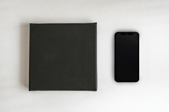 Black square clean canvas for photography or drawing lies on a white background next to a black smartphone (974)