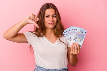 Young caucasian woman holding bills isolated on pink background  showing a dislike gesture, thumbs down. Disagreement concept.