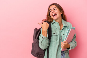 Young caucasian student woman holding books isolated on pink background  points with thumb finger away, laughing and carefree.