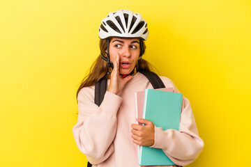 Young caucasian student woman wearing a bike helmet isolated on yellow background  is saying a secret hot braking news and looking aside