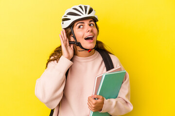 Young caucasian student woman wearing a bike helmet isolated on yellow background  trying to listening a gossip.