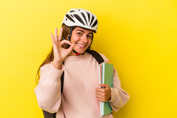 Young caucasian student woman wearing a bike helmet isolated on yellow background  cheerful and confident showing ok gesture.