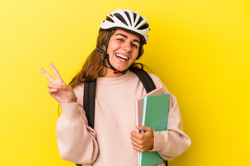 Young caucasian student woman wearing a bike helmet isolated on yellow background  joyful and carefree showing a peace symbol with fingers.