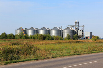 Grain elevator in rural zone. Modern agricultural grain elevator with blue sky on the background and roan on foreground.