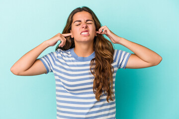Young caucasian woman isolated on blue background  covering ears with fingers, stressed and desperate by a loudly ambient.