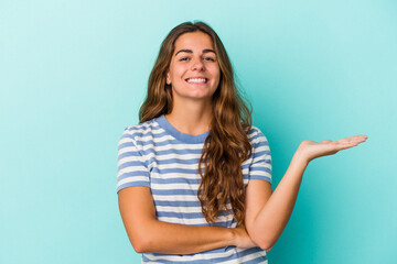 Young caucasian woman isolated on blue background  showing a copy space on a palm and holding another hand on waist.