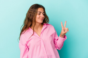 Young caucasian woman isolated on blue background  joyful and carefree showing a peace symbol with fingers.